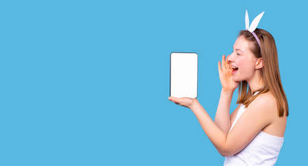 Shiny girl wearing the hoop with hare ears shouts covering the mouth in the side with the hand and bend her arm in the log holding the tablet on the palm.の写真素材