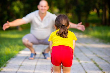 The back view photo of a nice daughter in yellow t-shirt and red shorts is gonna run to her daddy who wants to embrace his girl.の写真素材