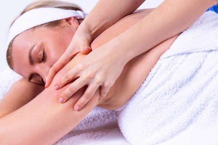 Close up photo of a woman being in a spa salon lying on the massage table with her hands under her head with closing eyes, undergoes a shoulder massage.の写真素材