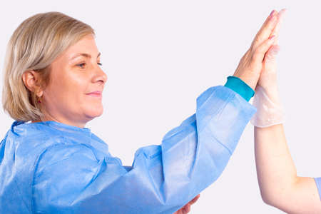 Profile photo of a woman in a blue medical gown preparing for surgery gives high five to a nurse wearing protective gloves with hand clap for good luck.の写真素材