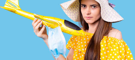 Summer time vacation the girl in a yellow polka-dot dress and the beach hat holding the plane toy with the medical mask.の写真素材
