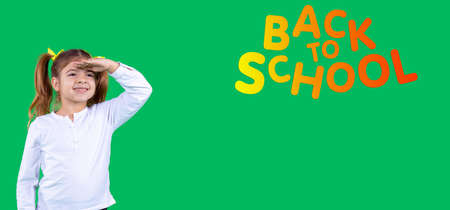 Banner, long format. Pretty school aged girl looks into the distance on a green background, holding her hand on her forehead. Side space.の写真素材