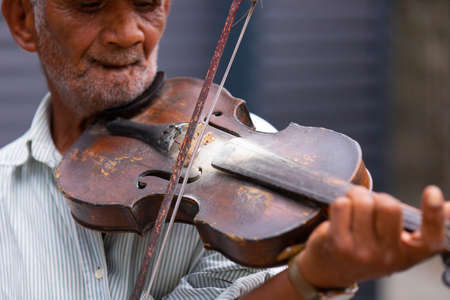 Closeup shot of an aged musician with wrinkled unshaven face playing the violin wonderful melody being on the street.の写真素材