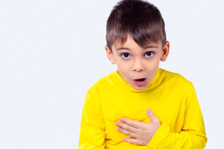 Close up photo of a boy with surprised face expression in yellow long-sleeved turtleneck holds his hand on his chest.の写真素材