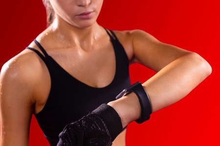 Close up photo of a sportive athletic girl wearing short top, sports gloves black color looking at the watch on the hand.の写真素材