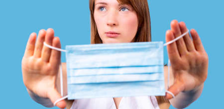 Close up photo of a young blonde woman looking up holding un her hands the medical disposable mask in pandemic time.の写真素材