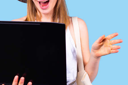 Surprised beautiful young blonde woman holding laptop open up taking her hand to the side palm forward.の写真素材