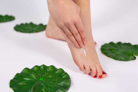 Close up photo of beautiful slim young lady legs with red pedicure moisturizes with cream her legs after epilation in the beauty salon.の写真素材
