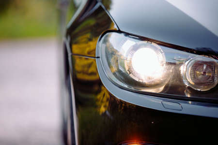 Cropped photo of a beautiful glossy black automobile on the road with headlights on, fog lights and part of a wheel.の写真素材