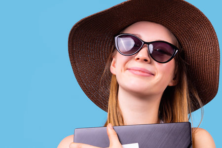 Happy smiling woman blonde wearing the brown summer hat in sunglasses holds the computer to her chest.の写真素材