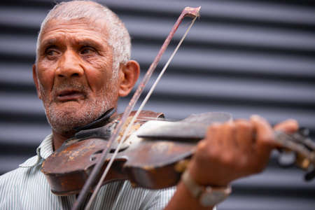 Close up photo of an old gray-hair man using violin playing a wonderful soulful melody outdoors turns his gaze to the side.の写真素材