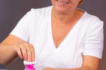 Senior smiling woman with acne disease using cotton pads and bottle of cosmetic lotion to wipe her face with acne points reducing irritation.の写真素材