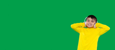 Joyful boy in yellow t-shirt holding on to headphones and listening the music very loudly over the green background.の写真素材