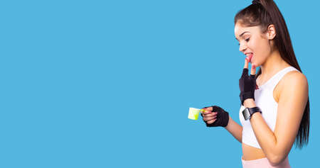 Beautiful close-up portrait of young sporty slim woman holding a small cup of ice-cream in one hand and tasting it with the index finger to the tongue.の写真素材