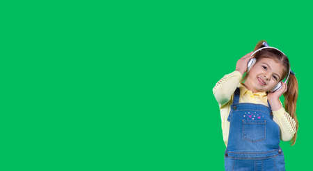 The little girl passionate about music is smiling and listening the music holding to headphones on her head.の写真素材