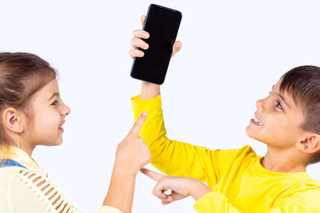 Two nice kids boy and girl fighting for the smart phone, the boy holding the phone in his hand and the girl wants to take it .の写真素材