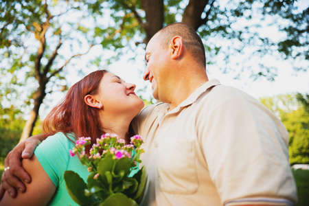 Happy couple in love having romantic date outdoors looking at each other and smiling, man gave his woman he loves flowers and embracing her.の写真素材