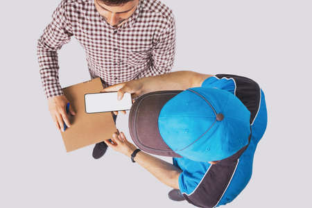 Photo from above of two men, client received the parcel and postman holding the cellphone in his hand for client to sign.の写真素材