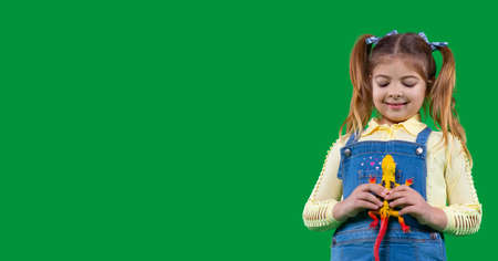 Beautiful smiling little girl holding a dinosaur toy yellow color in her hands and is looking at it.の写真素材