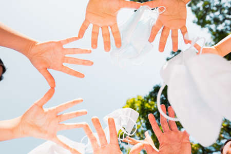 Photo bottom view of the people palms holding each other with the little fingers and thumbs meanwhile throwing medical masks in the air.の写真素材
