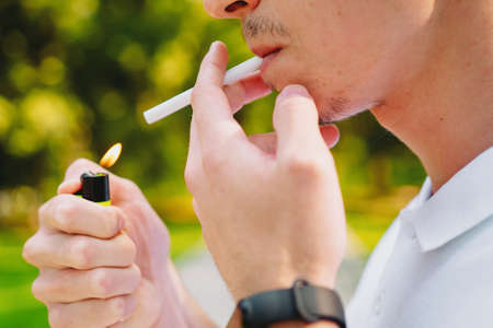 Cropped side view photo of a student man wearing smart watch on his hand and smokes a cigarette outdoors, having addicted nicotine problems.の写真素材