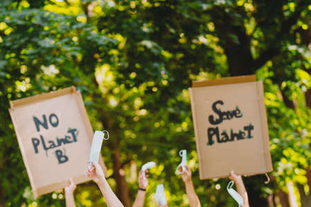 Homemade poster at environmental rally in the green park, people protesting over pollution and global warming, to save planet earth, on pandemic time raising up medical masks.の写真素材