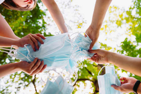 Close up portrait from below of people holding their medical and surgical mask in their hands in the center togetherness, quarantine freedom concept and lifestyle. being outdoors,の写真素材