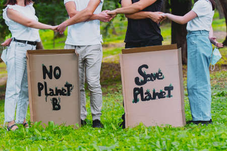 Cropped photo of two couples outdoors holding hands with cardboards posters with the inscription about saving nature, two young women keep medical masks in the hands behind their backs.の写真素材