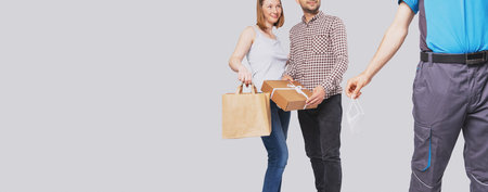 Cropped photo of a beautiful young couple holding a carton package and a parcel in their hands, delivery man holding a medical mask in his hand.の写真素材