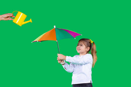 The nice girl with two tails in white shirt is holding colorful umbrella and somebody holding a watering can.の写真素材