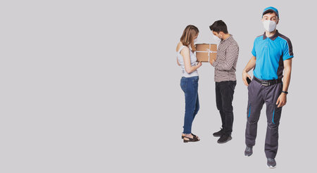 Side copy space photo of a couple received the package and they looking at it, the postman putting the mobile phone in the pocket, all in medical mask.の写真素材
