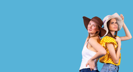 Two amazing young women wearing the hats standing back to back each other and looking up with smiling face.の写真素材