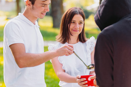 Photo of two kindness people, young smiling woman and a man giving some food to a homeless man, volunteer mission.の写真素材