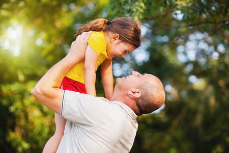 Close up photo of a daddy raising his little daughter up and the are happy spending a beautiful sunny day together outdoors.の写真素材