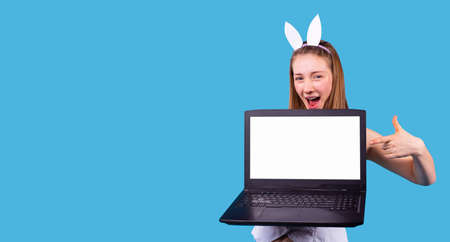 Smiling broadly young woman wearing the hoop with hare ears holding the laptop opened and pointing at it.の写真素材