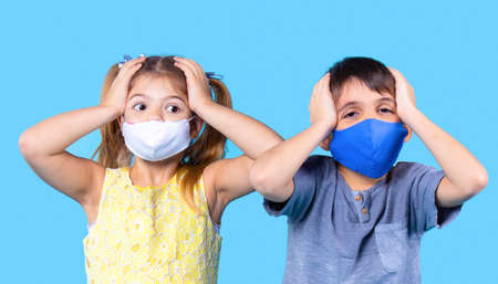 Close up portrait of two tired children, brother and sister, wears protective masks and they are holding on to the head.の写真素材