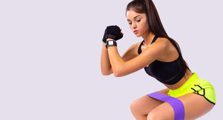 Sporty pretty woman in sports clothes does exercise workout with elastic rubber bandage gum poses indoors.の写真素材
