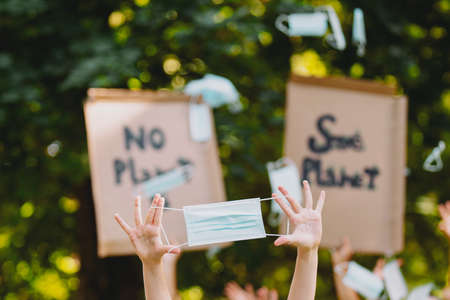 Blurry photo of two cardboard posters with the inscriptions of saving our planet earth from the pollution and in the foreground someone holds the medical mask in the hands.の写真素材