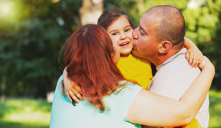 Young smiling family with child having fun together, loving couple holding their joyful daughter in their hands and kissing her on her cheeks.の写真素材