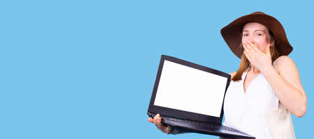 Woman with shocking facial expression covers her mouth using the hand and holding the opened laptop in the other hand.の写真素材