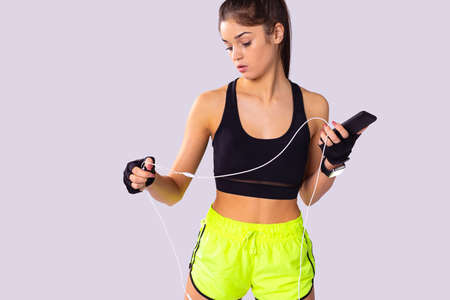 Attractive fitness young woman standing in short top and sports shorts straighten the wire from the headphones and holding the phone in her left hand.の写真素材