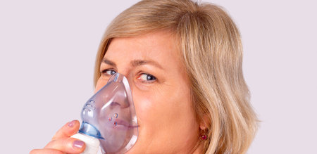 Close up photo of a blonde woman holding on her face the oxygen mask to improve breathing on...