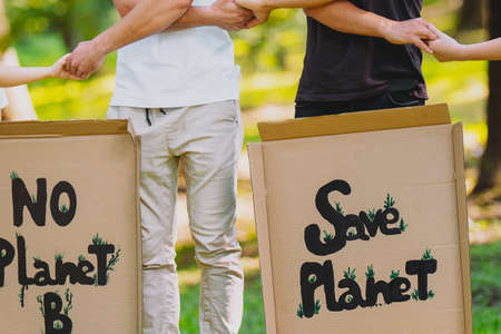 Cropped photo of of two men with cardboard posters holding hands with their friends made a circle in support of nature conservation.の写真素材