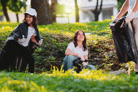 Community project, volunteer mission for gathering rubbish in the park using gloves and garbage bags, one girl making fun and smiling.の写真素材