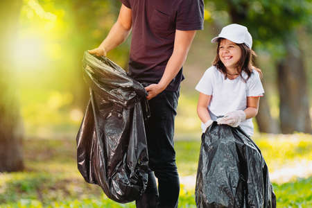 Team of two people, smiling girl and a man participate in mission clean to protect nature from the garbage using gloves and black bags.の写真素材