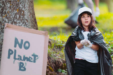 Picture of a girl in protective gloves with a garbage bag over her shoulders and a cardboard banner near the girl with an inscription as a sign not to pollute the earth.の写真素材