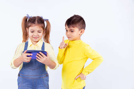 Beautiful smart happy girl holding the smart phone in her hands and playing the game and attentive boy shows with an index finger that it is forbidden to take the cellphone.の写真素材