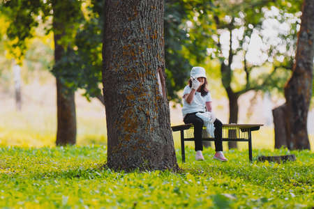 Young beautiful girl volunteer in black and white clothes sitting on a bench close to a tree tired and resting after work for gathering garbage and raised her hand up showing two fingers up.の写真素材
