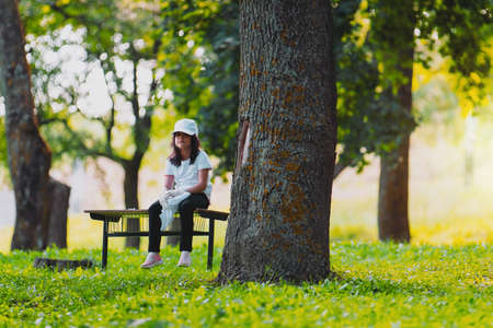 Close up photo of a beautiful volunteer girl sitting alone on a bench near a tree and resting outdoors wearing black and white clothes, volunteer mission for making nature clean and save.の写真素材