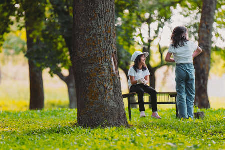 Close up photo of two girls outdoors, one girl posing standing with the back to the camera and another girl is sitting on a bench, resting after voluntary work for gathering garbage.の写真素材